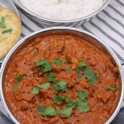Slow cooker chicken tikka masala in balti dish with coriander and nigella seeds with rice and naan bread in background