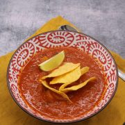 Spicy chilli bean soup in red and white bowl with tortilla crisps and lime wedge