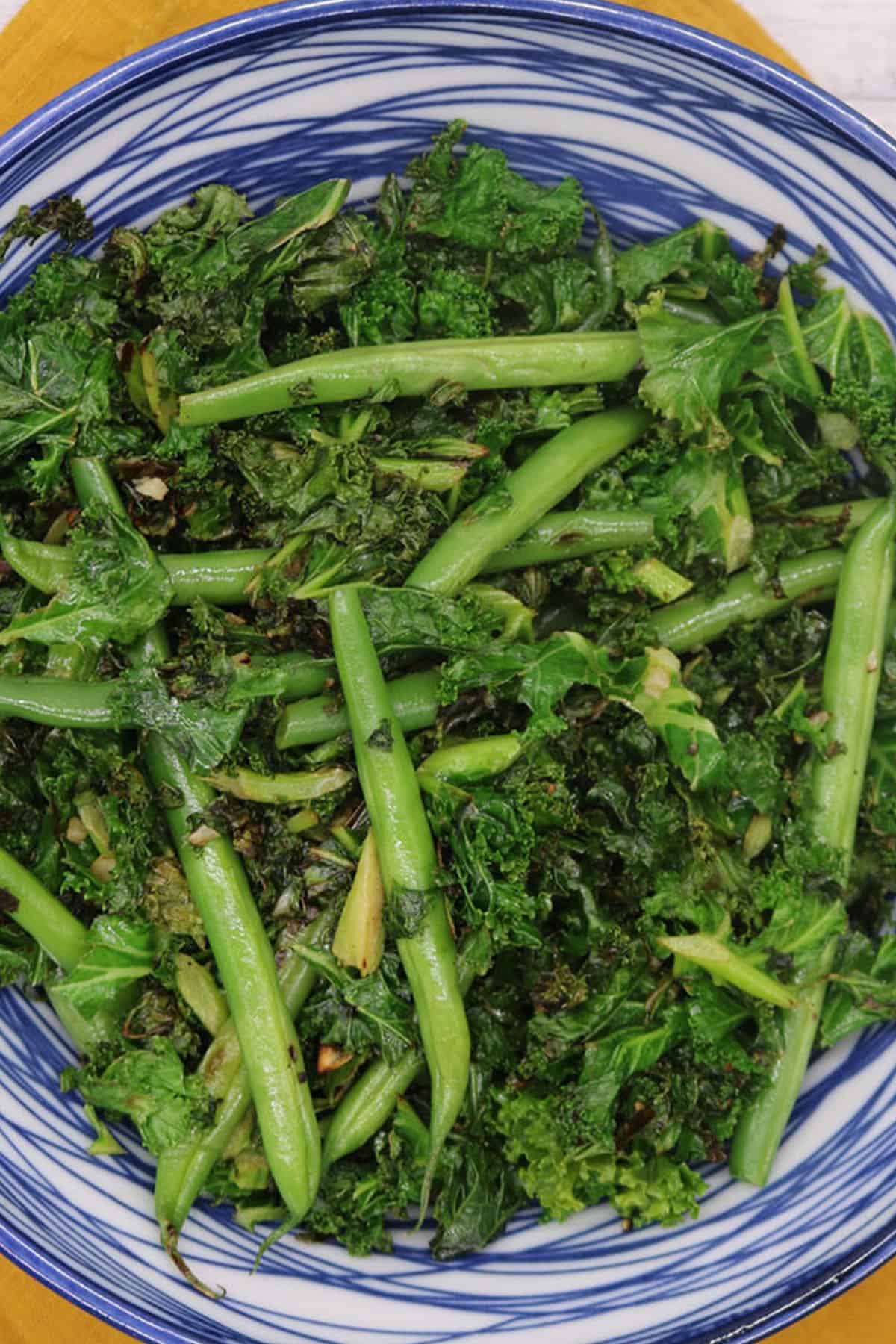 Close up photo of sauteed kale and green beans in a blue and white bowl