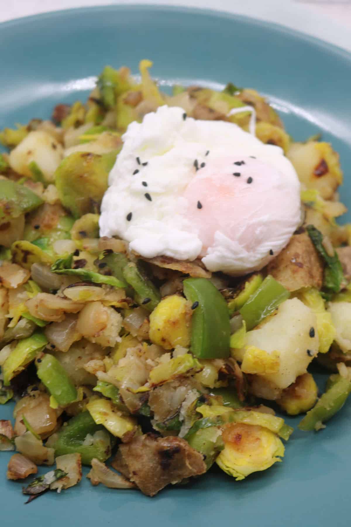 Winter breakfast hash topped with poached egg in green bowl