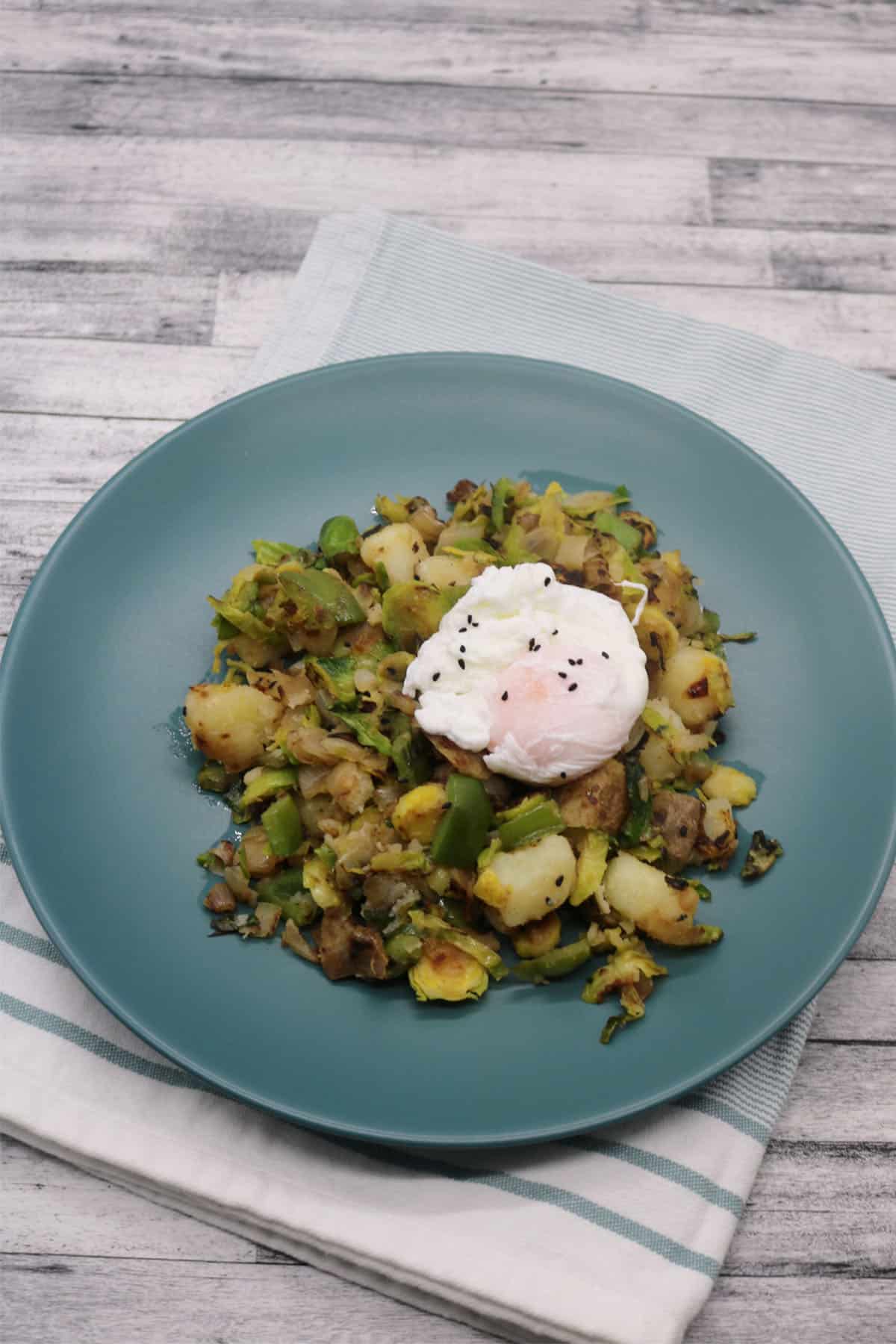 Winter breakfast hash topped with poached egg in green bowl sitting napkin