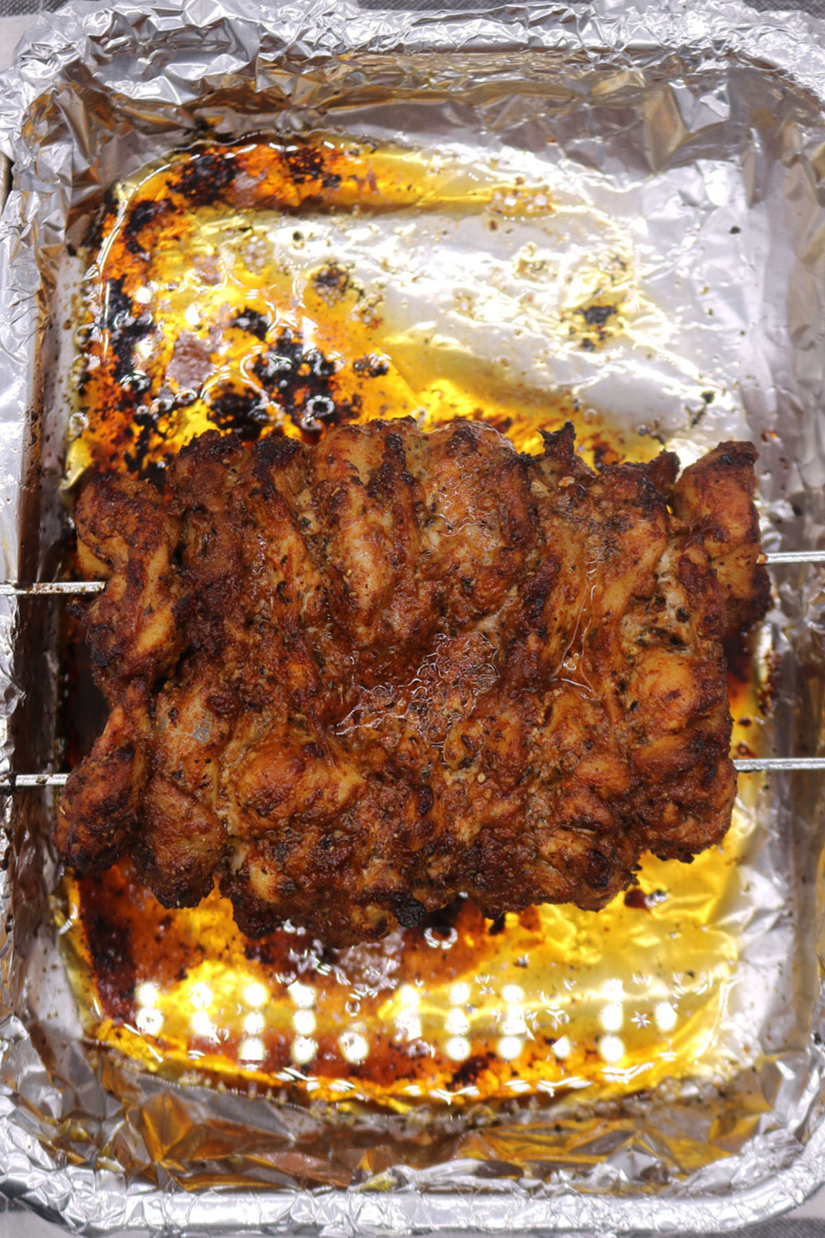 Chicken gyros meat on skewers in roasting tin with foil