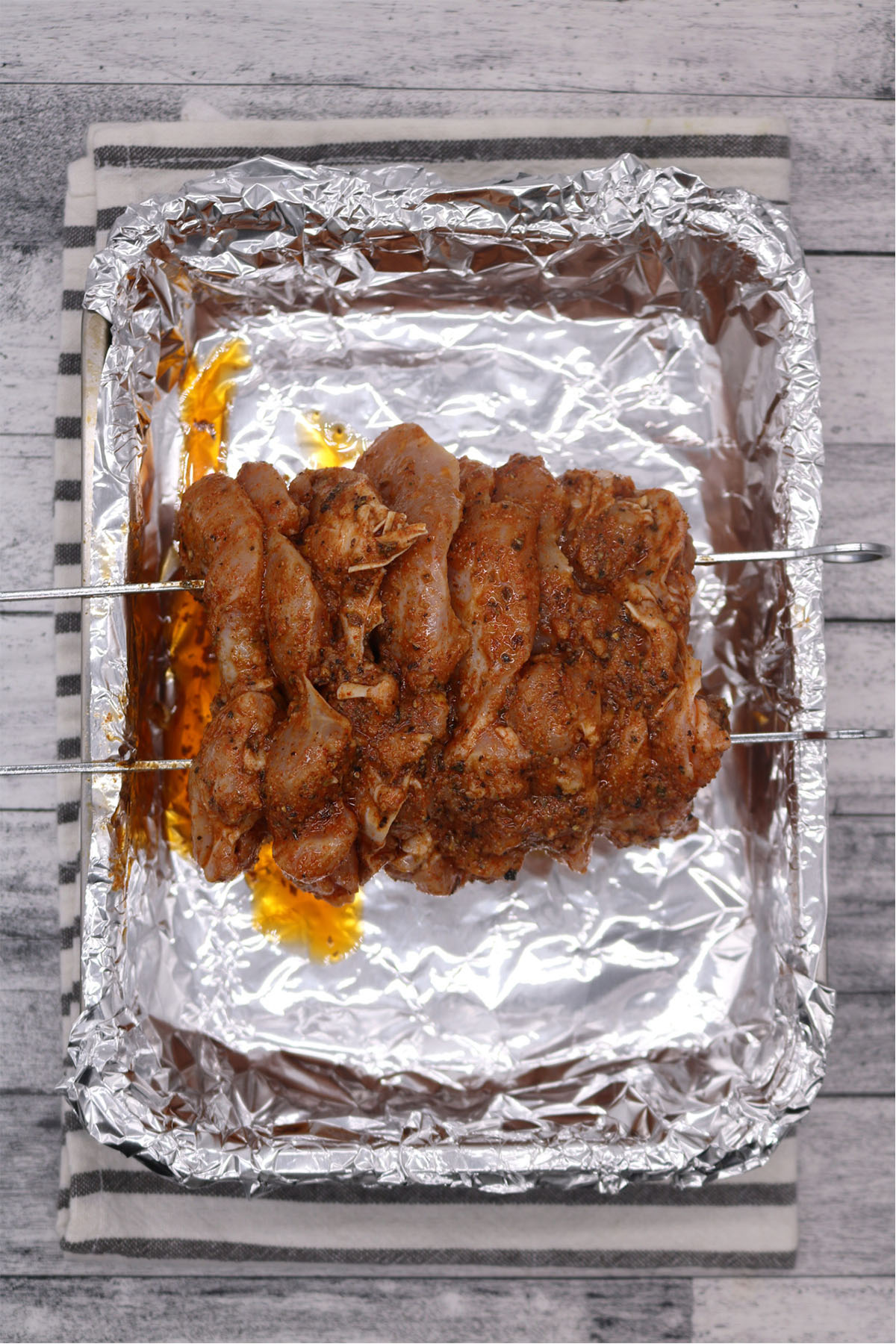 Raw Chicken gyros meat on skewers in roasting tin with foil