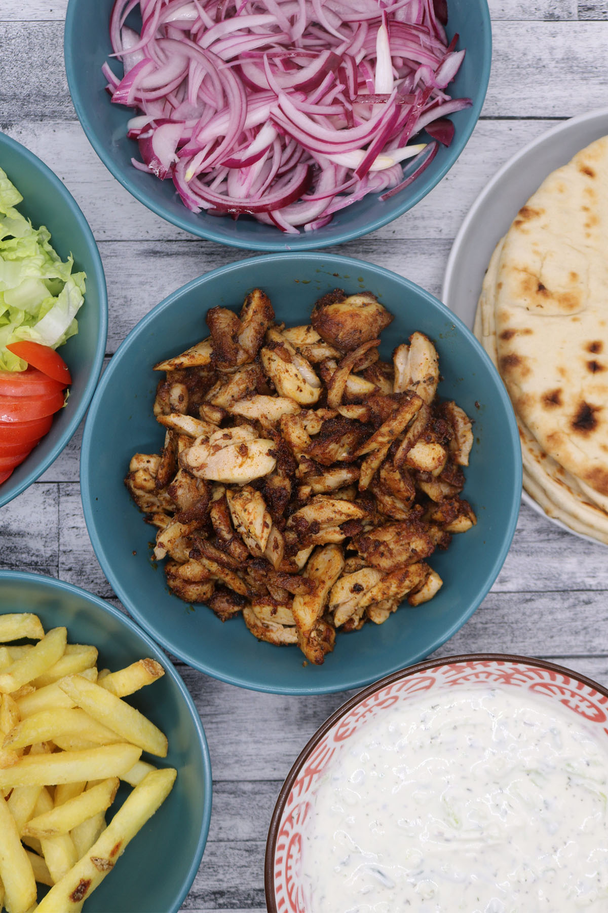 Chicken gyros in green bowl with accompaniments around outside