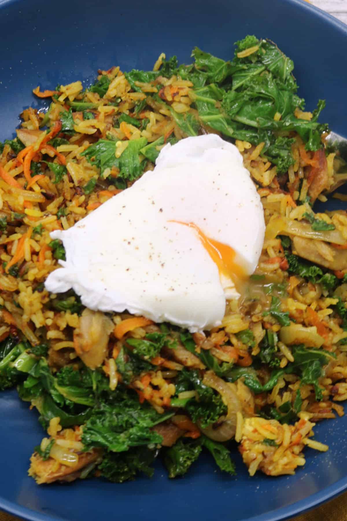 Spiced kipper fried rice topped with poached egg in blue bowl with fork