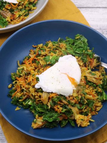 Spiced kipper fried rice topped with poached egg in blue bowl sitting on yellow napkin with fork