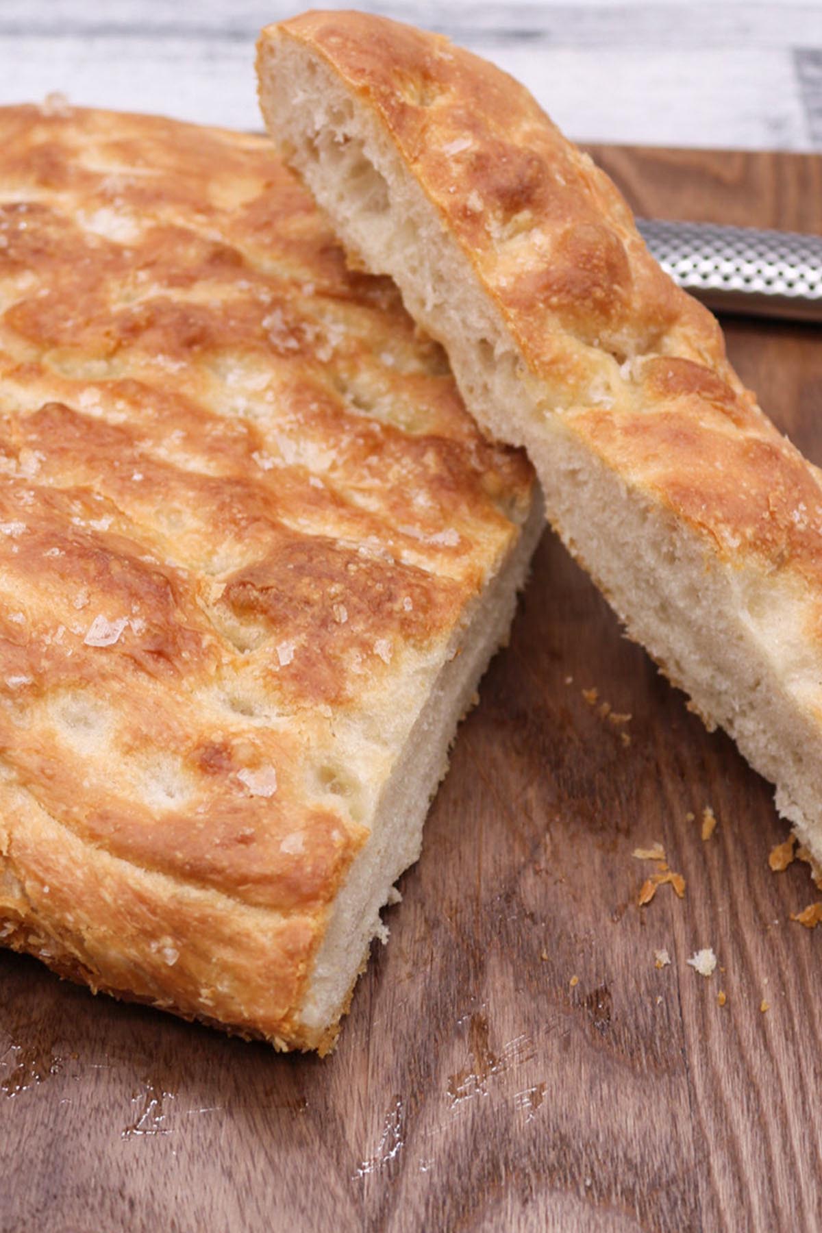 sliced focaccia on brown wooden chopping board with bread knife