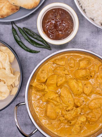Butter chicken in baltic bowl with crisps, naan, rice, mango chutney and green chillis