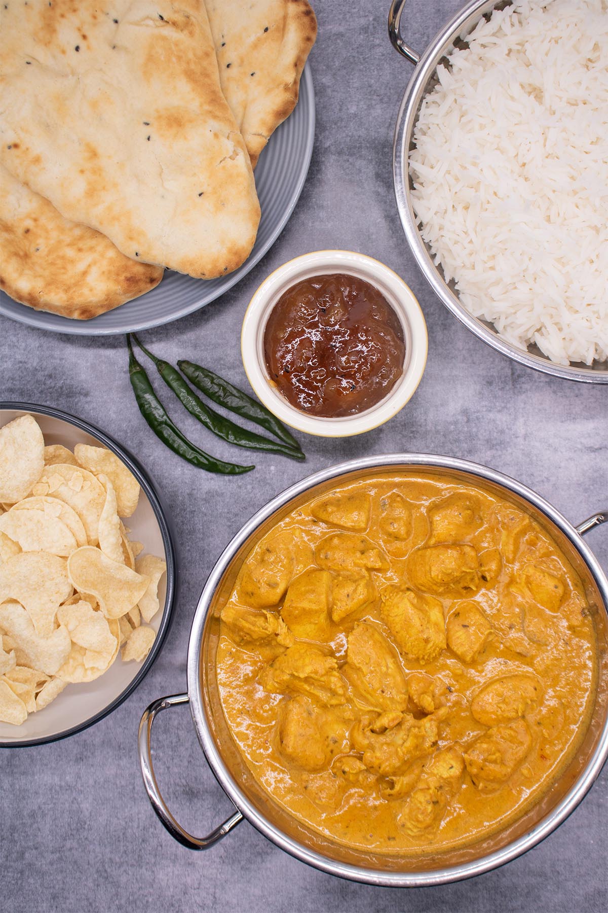 Butter chicken in baltic bowl with crisps, naan, rice, mango chutney and green chillis