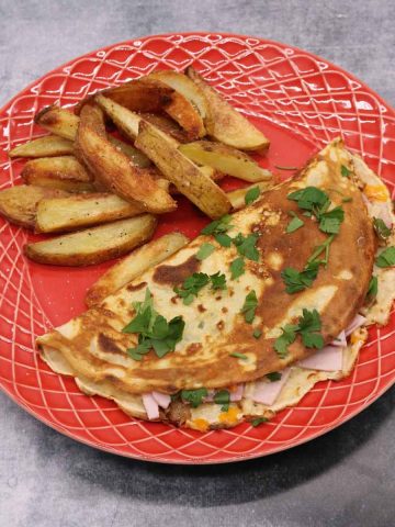 cheese and ham pancake on red plate with chunky chips