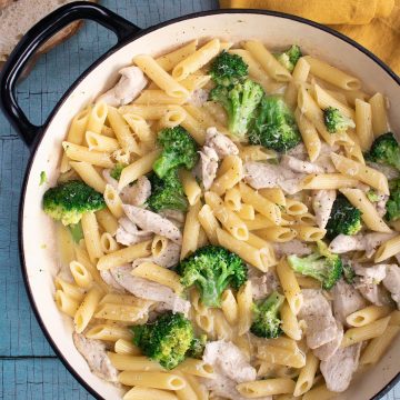 Chicken and broccoli pasta in large round casserole with bread and yellow napkin in background
