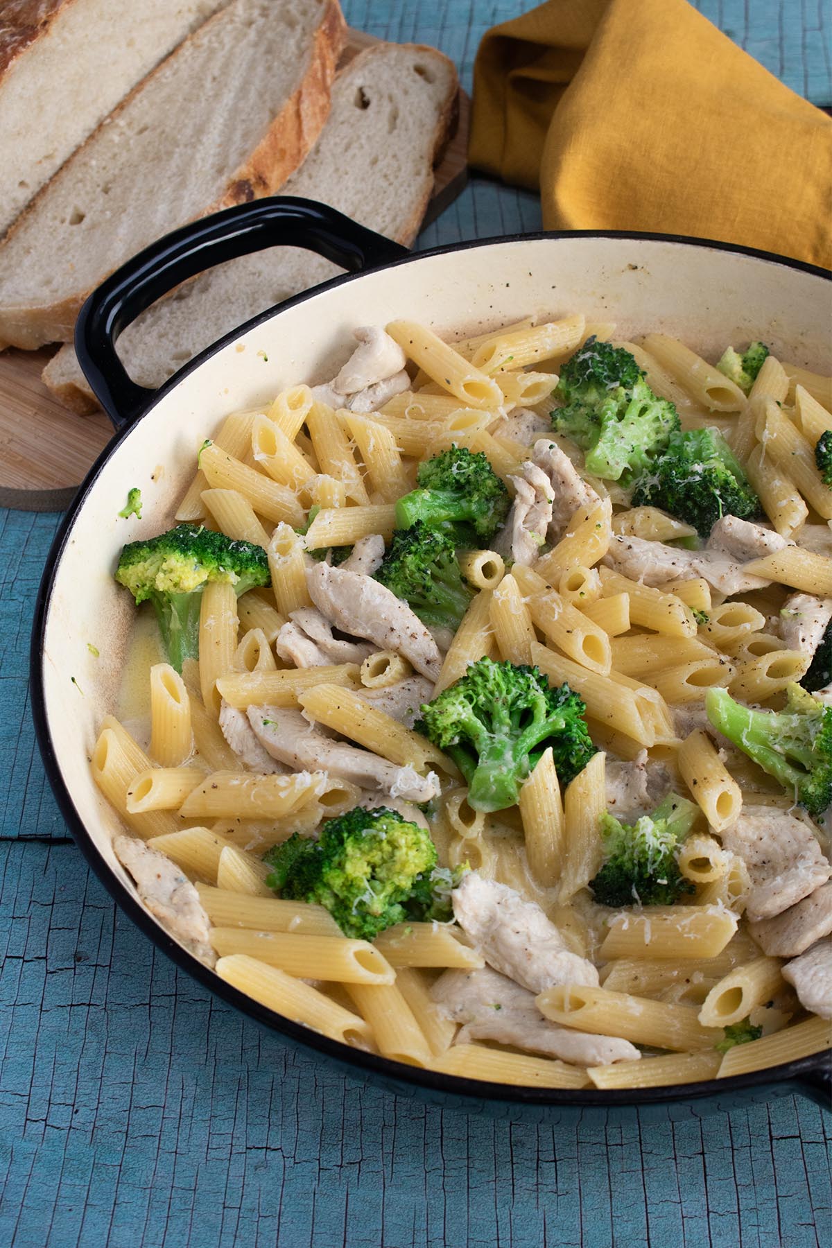 Chicken and broccoli pasta in large round casserole with bread and yellow napkin in background