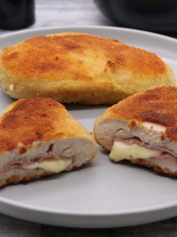 Two chicken cordon bleu on grey plate one sliced open showing ham and cheese