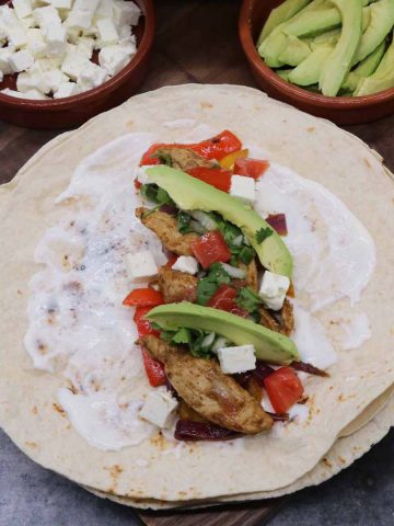 Chicken fajitas with avocado on tortilla with cheese, avocado and soured cream on the side