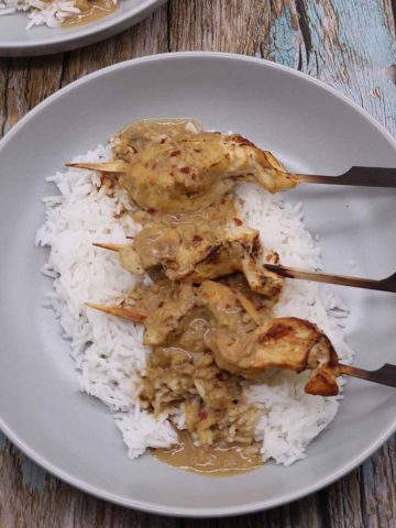 Chicken satay skewers on bed of rice in grey bowl