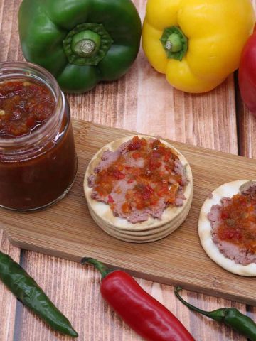 Board with crackers spread with pate and chilli jam, jar, peppers and chillis arranged around board