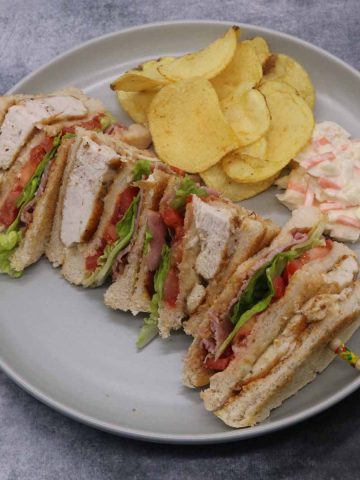 Club sandwich on grey plate with crisps and coleslaw