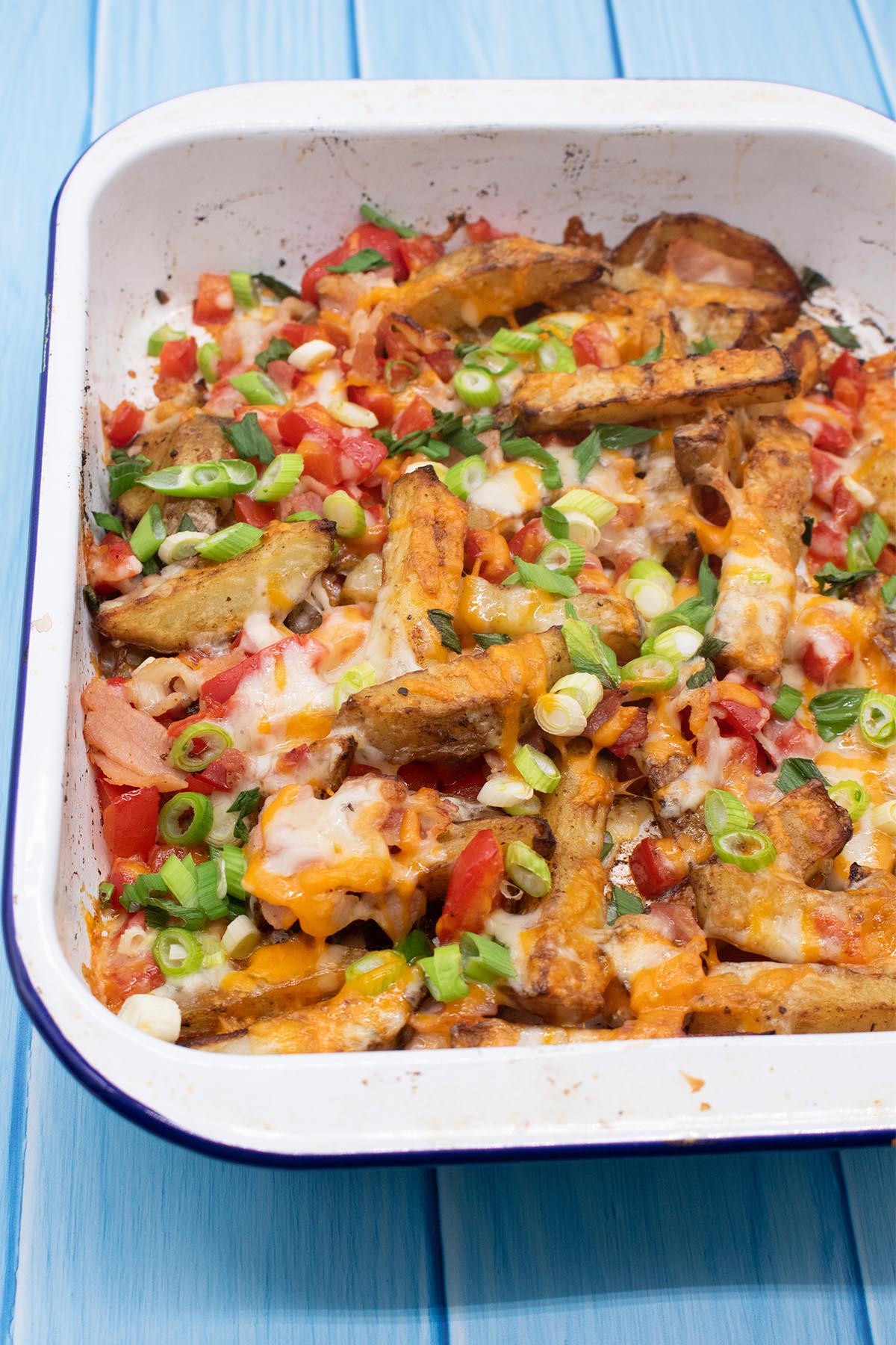Dirty fries covered in cheese, spring onions, bacon and pepper in a rectangle oven tray