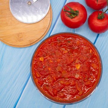 Pizza sauce in bowl with 3 tomatoes and pizza cutter