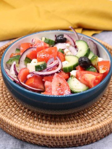 Greek salad in bowl sitting on basket with yellow napkin in background