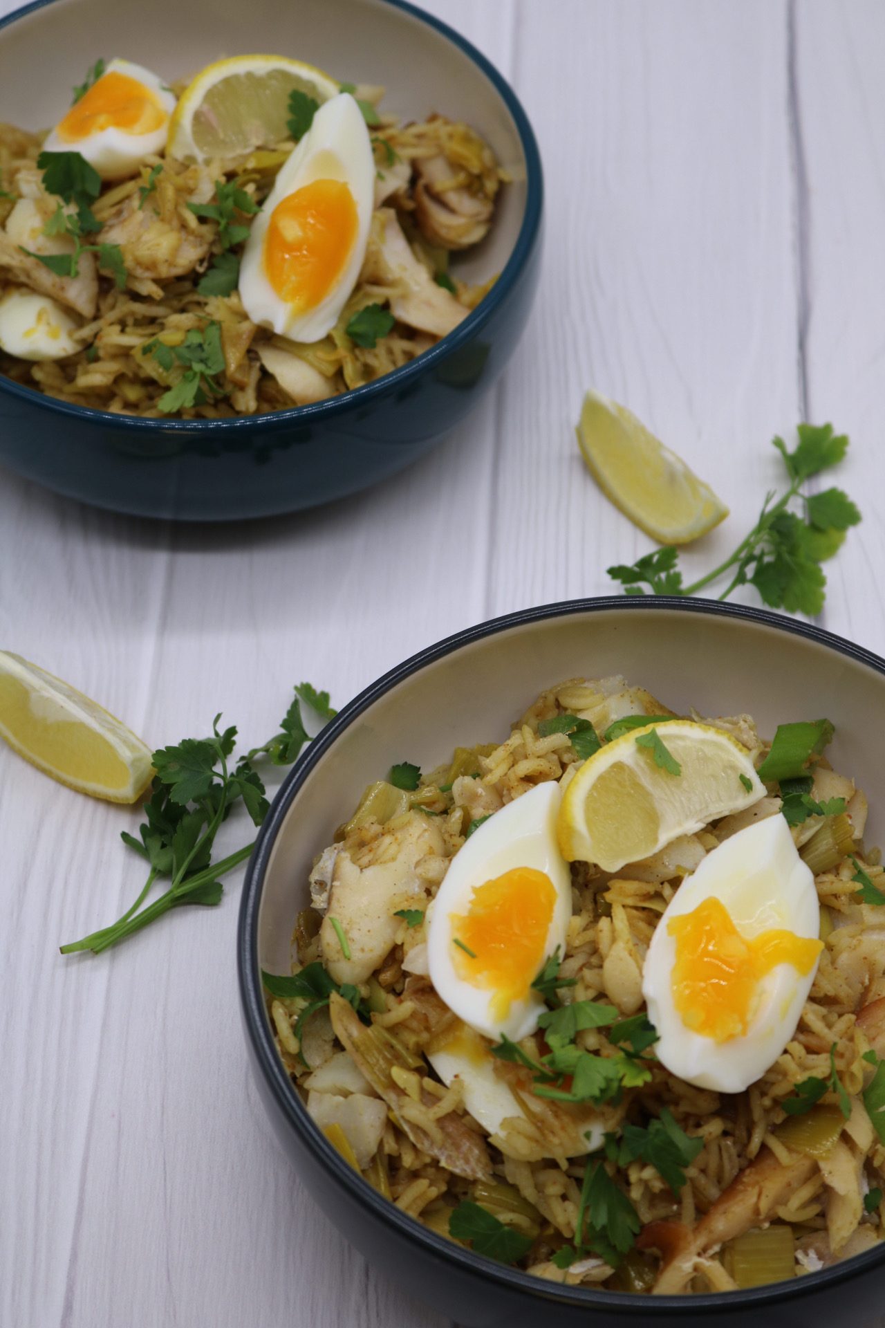 Kedgeree in two bowls with wedges of lemon and soft boiled egg