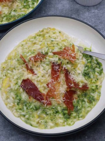 Leek risotto with kale pesto in bowl with shards of pancetta and fork