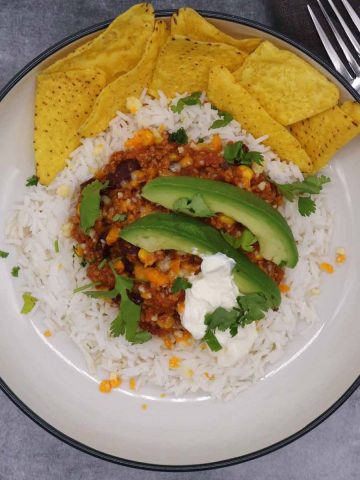 Mexican turkey chilli in a bowl with avocado, rice, tortilla chips, soured cream and coriander