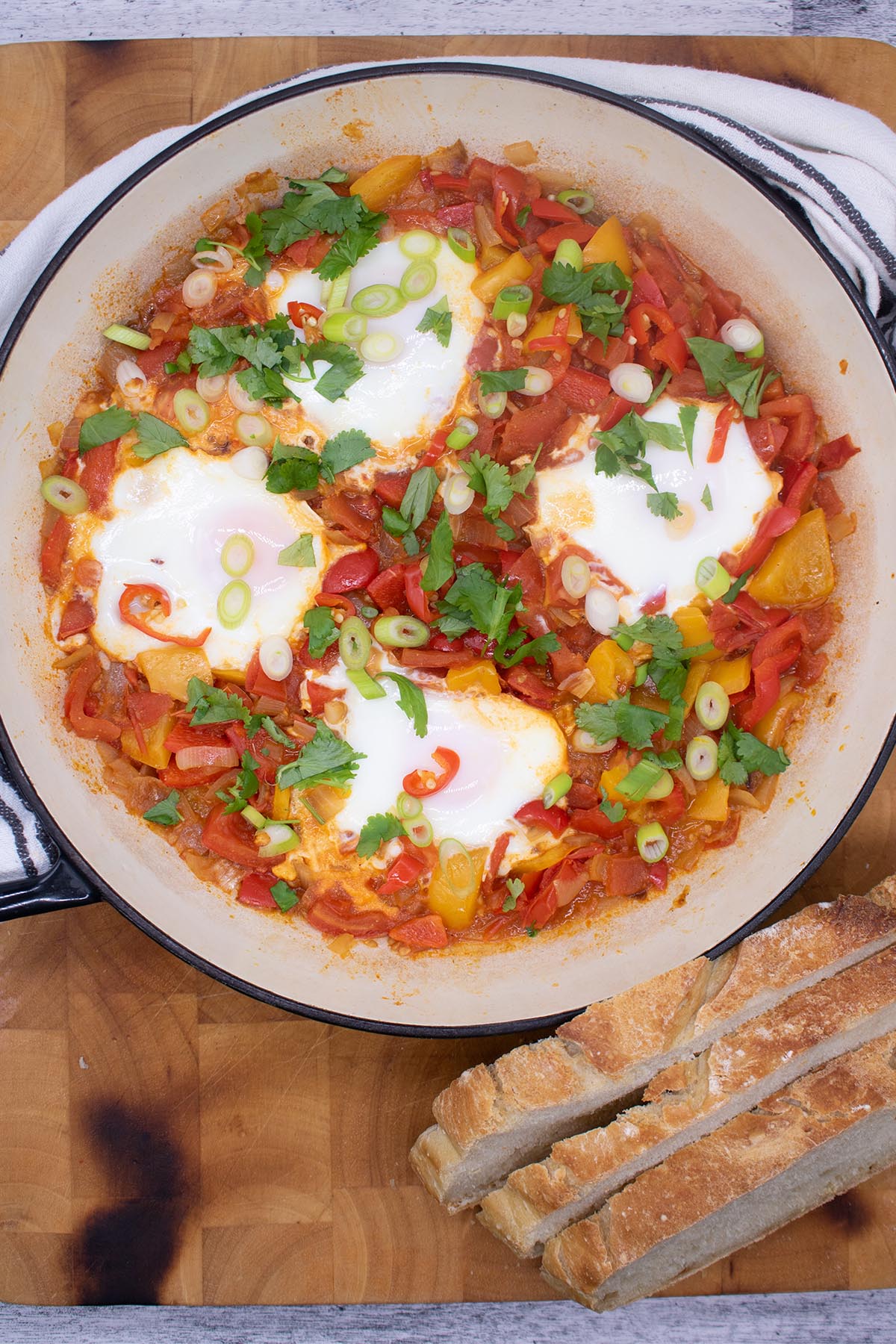 Eggs in a tomato and pepper sauce in a large round casserole with bread at the side