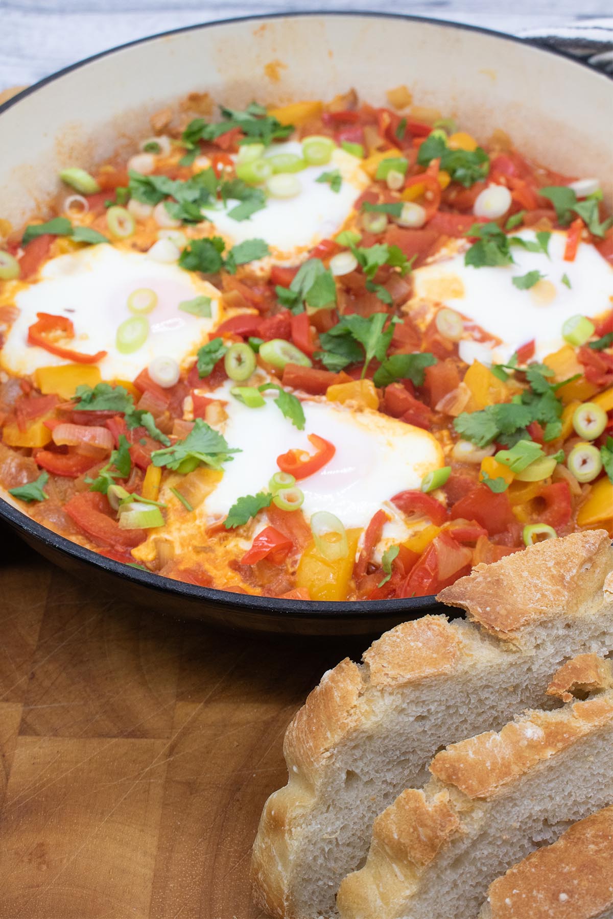 Eggs in a tomato and pepper sauce in a large round casserole with bread at side
