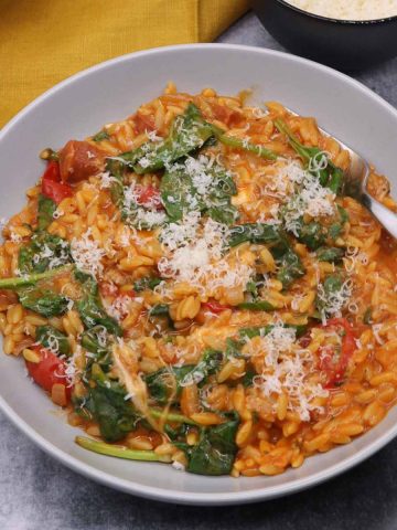 Orzo risotto with spinach in grey bowl with fork and parmesan