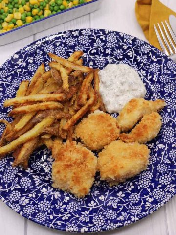 Panko cod cheeks, skinny oven chips and tartare sauce on bleu and white plate with fork and knife and yellow napkin