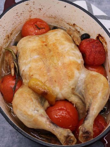 Whole chicken in oval casserole dish with tomatoes and rosemary