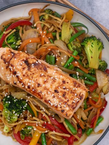 Salmon in a bowl with noodles and vegetables, chopsticks by the side