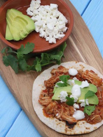 chicken tinga on flour tortilla on wooded board with cheese and avocado