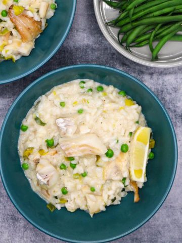 Smoked haddock risotto in a green bowls with wedge of lemon next to bowl of green beans