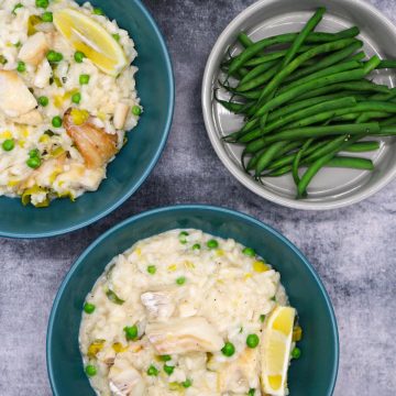 Smoked haddock risotto in a green bowls with wedge of lemon next to bowl of green beans and glass of white wine