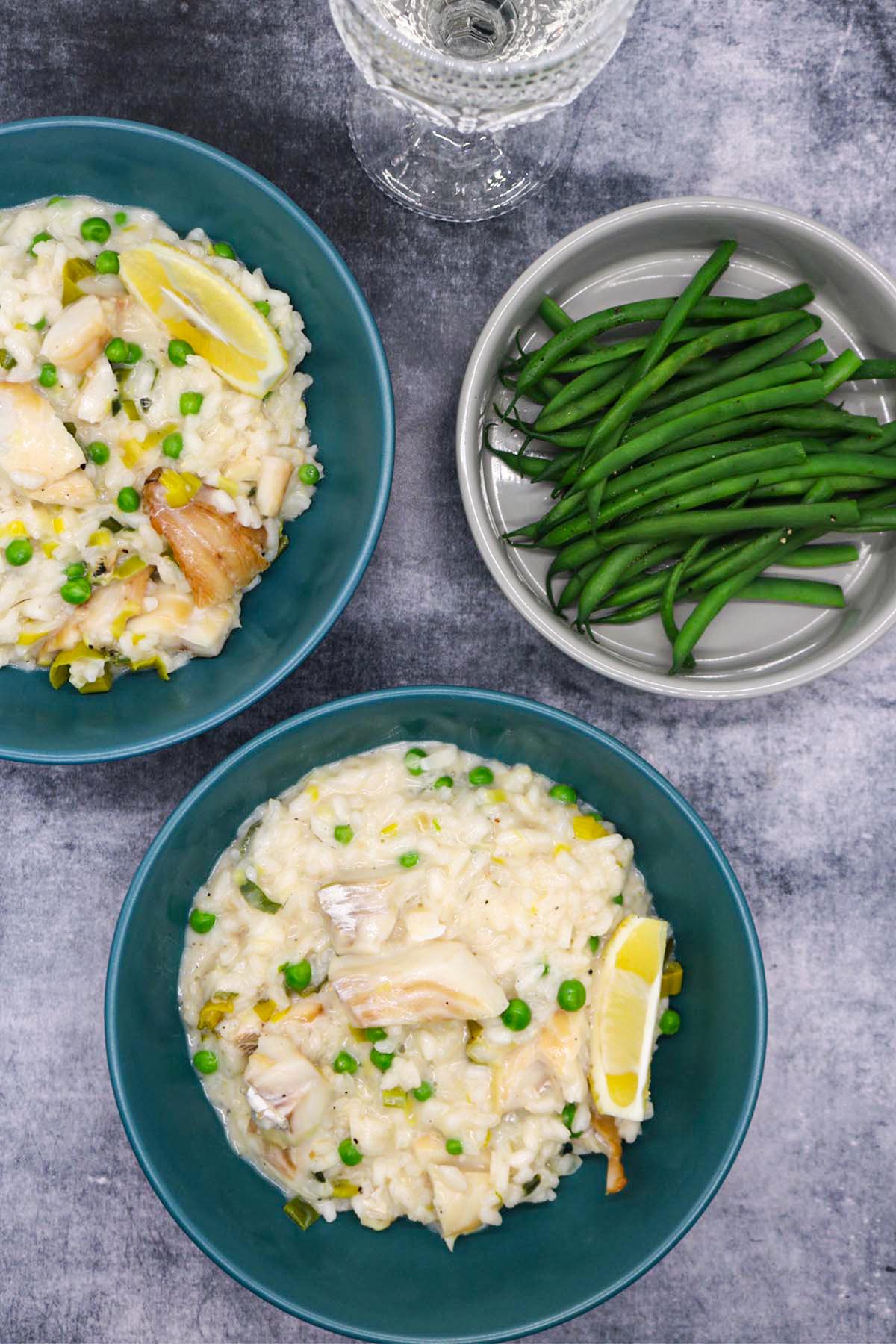 Smoked haddock risotto in a green bowls with wedge of lemon next to bowl of green beans and glass of white wine