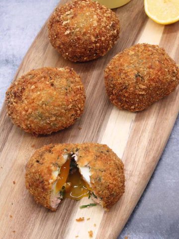 4 smoked salmon scotch eggs on wooden board with lemon halves