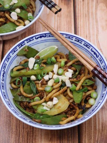 spicy pork and peanut noodles in a blue and white bowl with chopsticks
