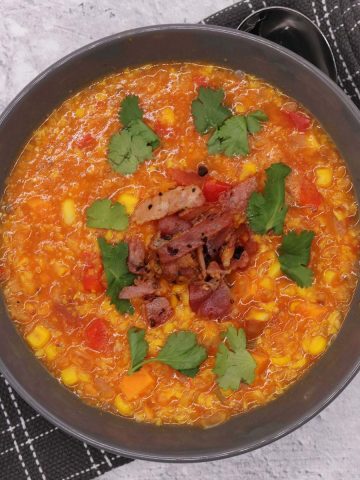 Spicy sweetcorn soup in grey bowl with bacon and coriander on top