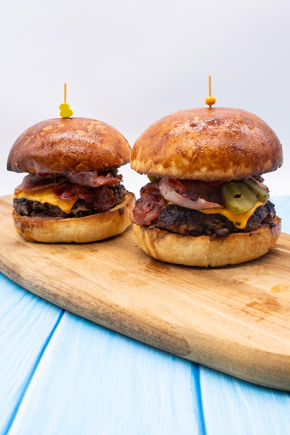 two steak and bacon burgers in brioche buns on wooded board
