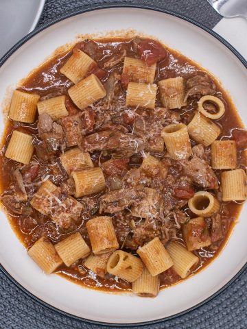 Venetian duck ragu in bowl with pasta, bread roll and fork in background