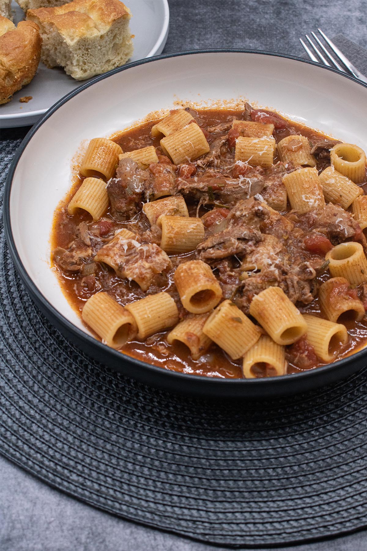 Venetian duck ragu in bowl with pasta, bread roll and fork in background