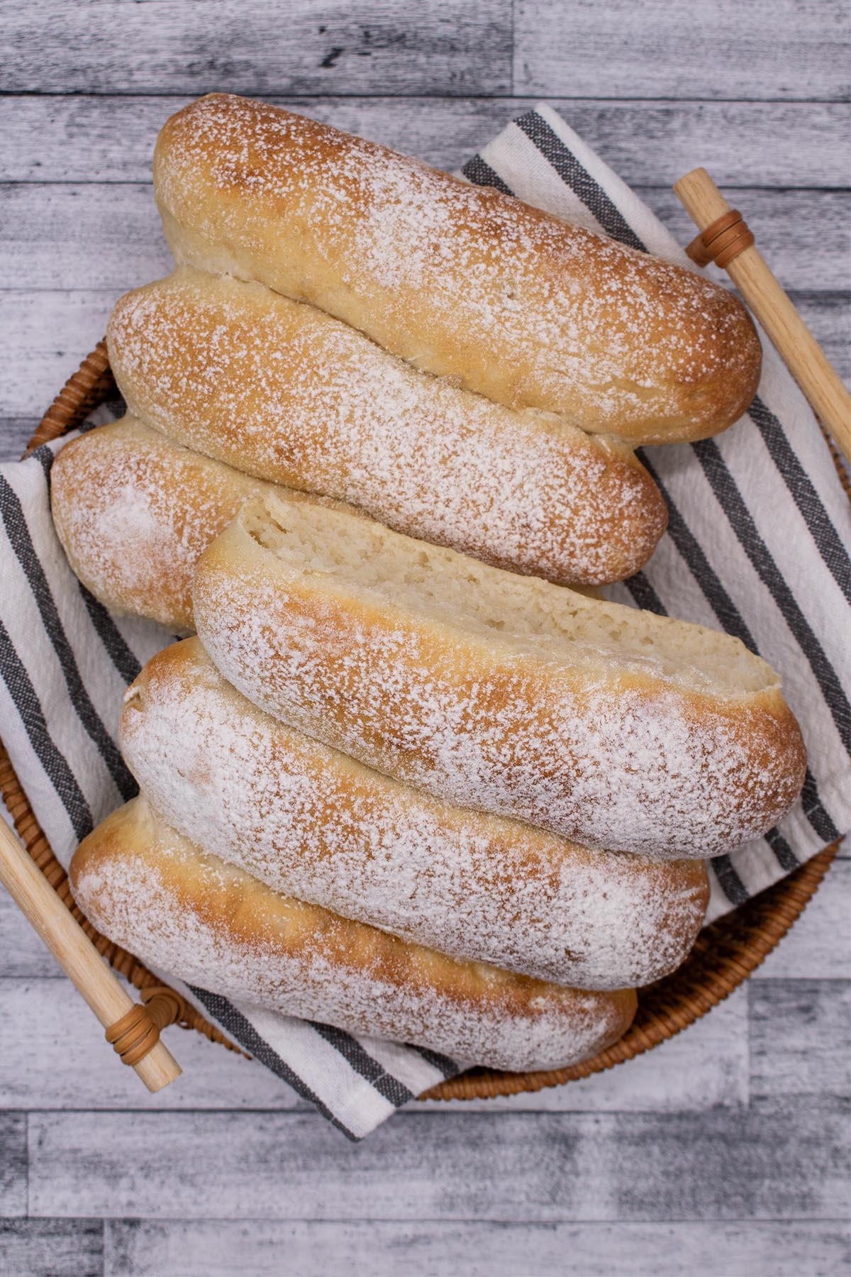 6 White finger rolls in a bread basket with a black and white towel