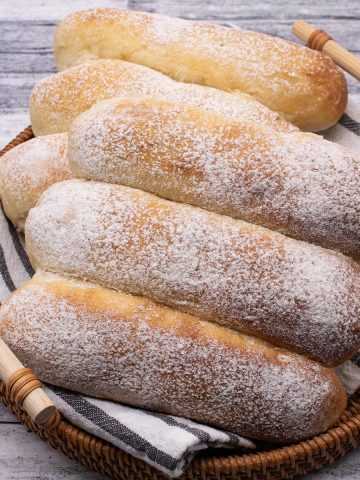 6 White finger rolls in a bread basket with a black and white towel