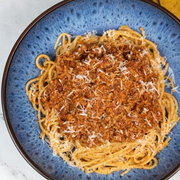Bolognese sauce served on spaghetti in a blue patterned pasta bowl with mustard napkin in the background