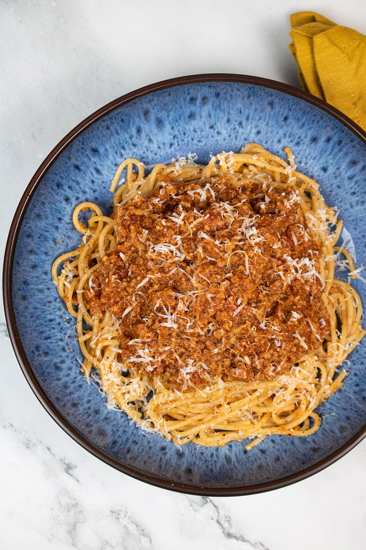 Bolognese sauce served on spaghetti in a blue patterned pasta bowl with mustard napkin in the background