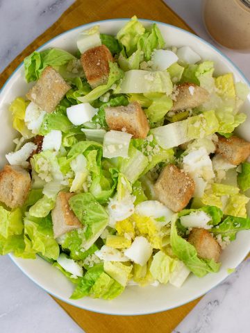Caesar salad in a serving bowl with jug of dressing on the side