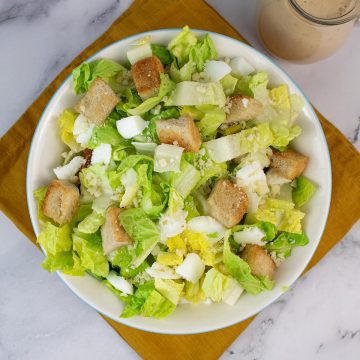 Caesar salad in a serving bowl with jug of dressing on the side