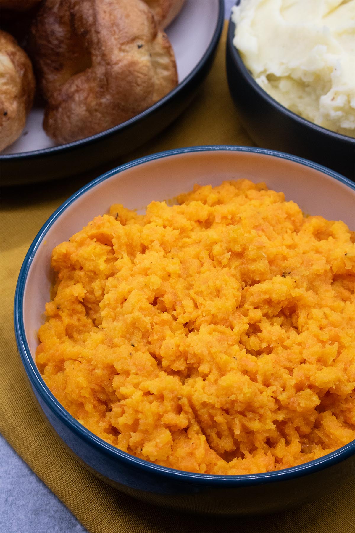carrot and swede mash, mashed potatoes and yorkshire puddings in bowls with orange napkin